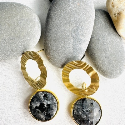 Brincos dourados com pedras pretas e cinza sobre pedras lisas cinza e bege