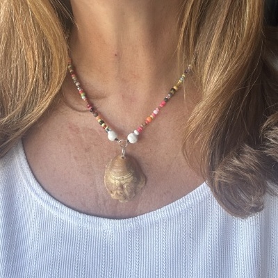 Colar colorido com concha pendurada em mulher com blusa branca.