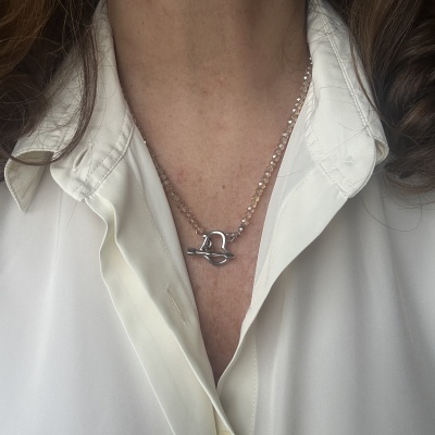 Colar com fecho metálico em forma de coração e seta, com contas transparentes rosadas, usado com camisa branca