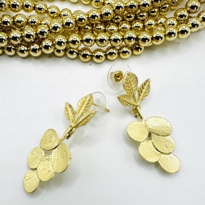 Brincos dourados em forma de folhas com colar de contas douradas no fundo branco