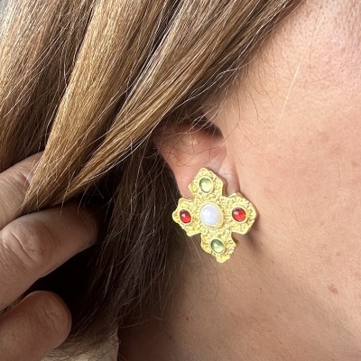 Brinco dourado de formato cruz com pedras coloridas na orelha