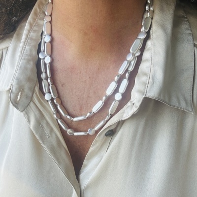 Colar prateado duplo usado sobre camisa bege clara