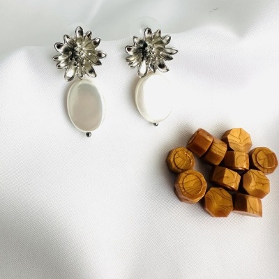 Brincos prateados com pendente branco e objetos de madeira sobre tecido branco