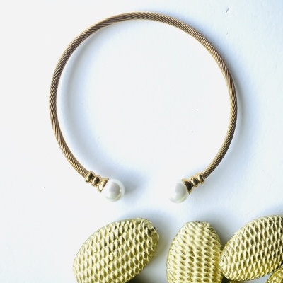 Bracelete dourado com pontas de pérola e contas ovais texturizadas em fundo branco