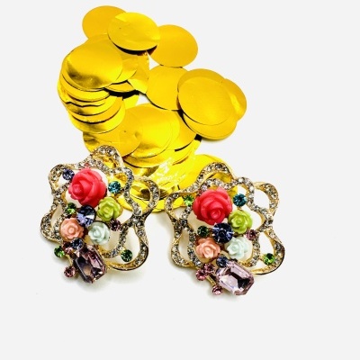 Par de brincos dourados com pedras coloridas e flores em resina sobre fundo branco e confetes dourados