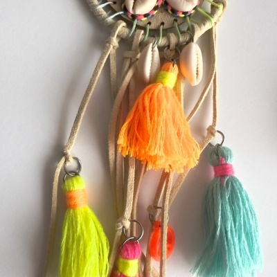 Objeto artesanal com búzios e pompons coloridos sobre fundo branco