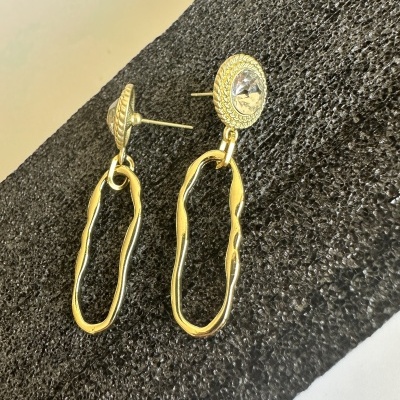 Brincos dourados com pedra clara sobre superfície preta