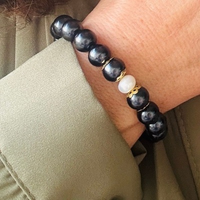 Pulseira de contas pretas e branca num pulso com camisa verde claro