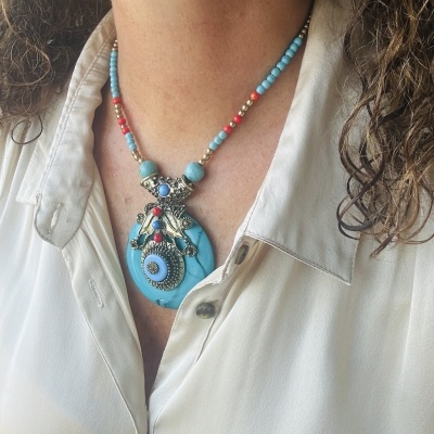 Colar colorido com pendente azul e detalhes prateados sobre camisa branca