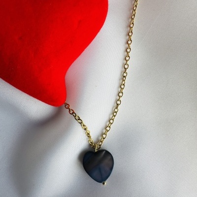 Colar dourado com pendente coração azul escuro sobre tecido branco e objeto vermelho coração
