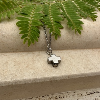 Colar com pendente de cruz prateada sobre superfície de pedra com folhas verdes