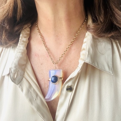 Colar dourado com pendente lilás e azul numa camisa bege clara