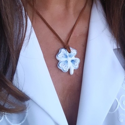 Colar com pendente de folha de quatro folhas branca com detalhes azuis e corda castanha, usado sobre camisa branca