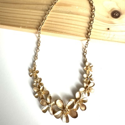 Colar dourado floral com pedras cristal em fundo branco e madeira