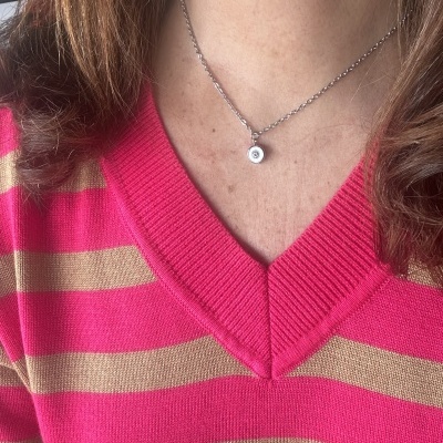 Colar prateado com pendente redondo branco e camisola de riscas cor-de-rosa e bege