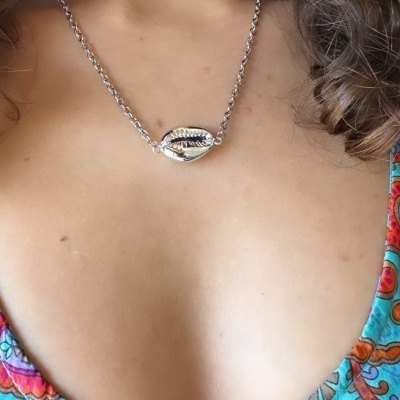 Colar prateado com pendente de concha no pescoço e blusa colorida com padrão floral