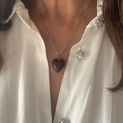 Colar com pendente coração castanho numa camisa branca com botões prateados
