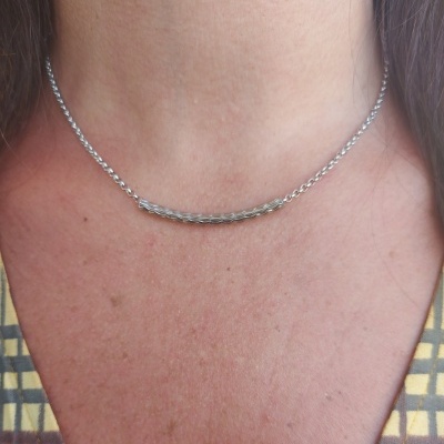 Colar prateado com tubo liso ao centro no pescoço