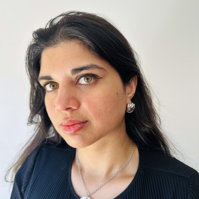 Mulher com brincos prateados e colar com pendente branco e preto, vestindo blusa preta.