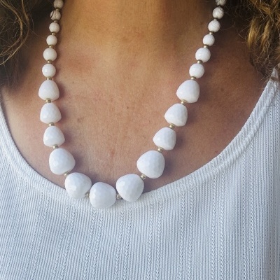 Colar de contas brancas triangulares e redondas com espaçadores dourados sobre camisa branca texturizada