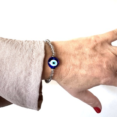 Pulseira de vidro com olho grego azul no pulso de uma mão com unha vermelha.