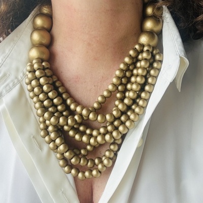 Colar dourado de várias voltas com contas grandes e pequenas sobre camisa branca