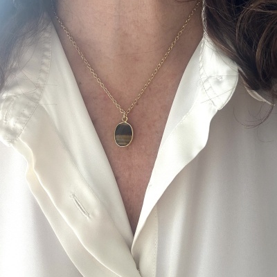 Colar dourado com pendente oval de pedra em tons marrons e dourados sobre camisa branca