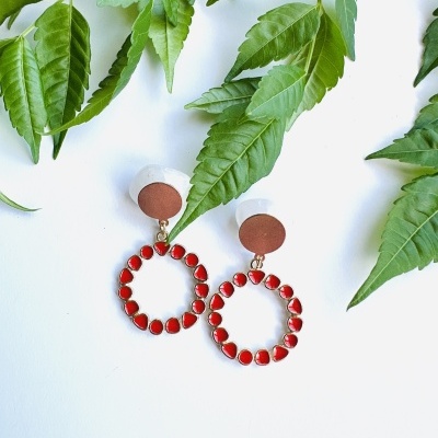 Brincos com pedras vermelhas em fundo branco e folhas verdes