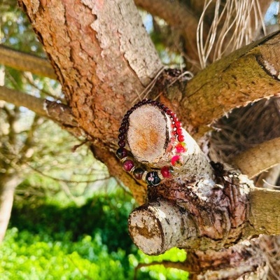 Pulseira de contas vermelhas, pretas e brancas numa árvore com ramos cortados ao ar livre