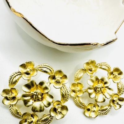 Brincos dourados em forma de flores com prato branco e dourado ao lado