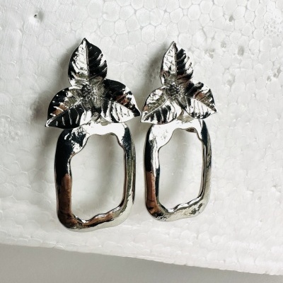 Brincos prateados em forma de folhas sobre base branca de isopor