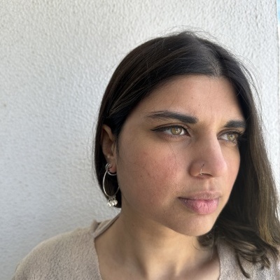 mulher com brincos de argola prateados e camisa bege perto de parede branca