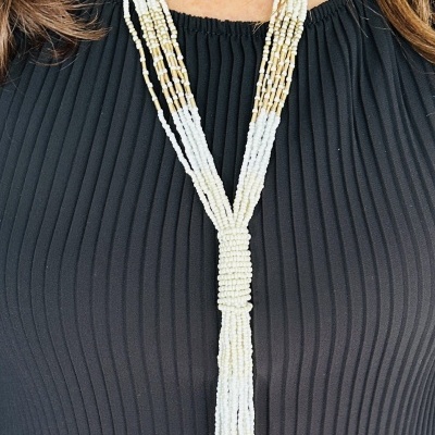 Colar longo de contas brancas e douradas com franjas sobre vestido preto plissado