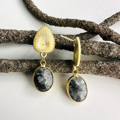 Brincos dourados com pedras pretas e brancas penduradas em ramos secos