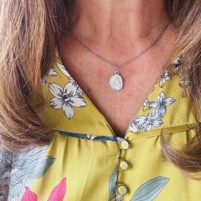 Colar com pendente oval prateado e vestido amarelo com padrão floral.