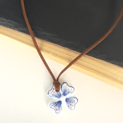 Colar com pendente de cerâmica em forma de flor e cordão castanho sobre fundo branco e madeira