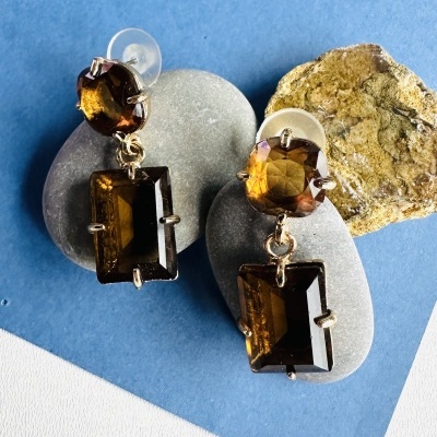 Brincos com pedras âmbar e castanhas sobre pedras e fundo azul