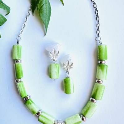 Conjunto de colar e brincos com contas verdes e prateadas e folhas ao fundo