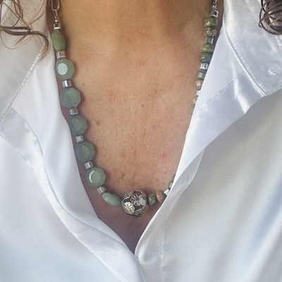 Colar de pedras verdes com pendente metálico sobre camisa branca acetinada