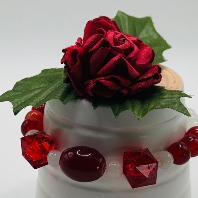 Pulseira vermelha com flor e folhas verdes sobre suporte branco