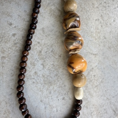 Colar com contas pequenas castanhas escuras e grandes bege e castanho marmorizadas sobre fundo cinza claro