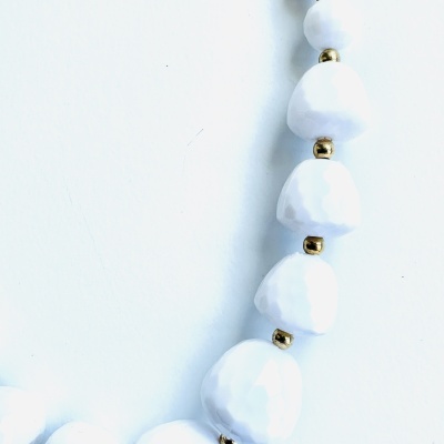 Colar com contas facetadas brancas e esferas douradas em fundo branco