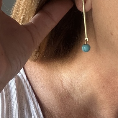 Brinco pendente dourado com bola azul em orelha de pessoa loira