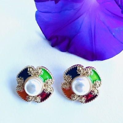 Brincos coloridos com pérola e dourado, sobre fundo branco e flor roxa