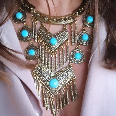 Colar grande dourado com pedras azuis usaudo sobre camisa branca