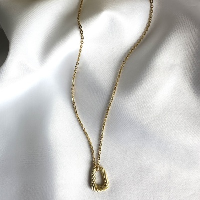 Colar dourado com pendente oval texturizado sobre tecido branco
