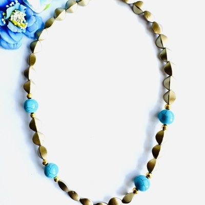 Colar dourado com contas azuis e flores azuis no fundo
