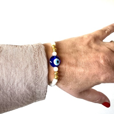 Bracelete com contas brancas, douradas e conta azul com olho no pulso