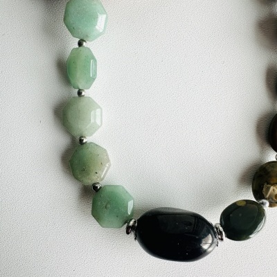Colar com pedras facetadas verdes e pretas sobre superfície branca e madeira clara