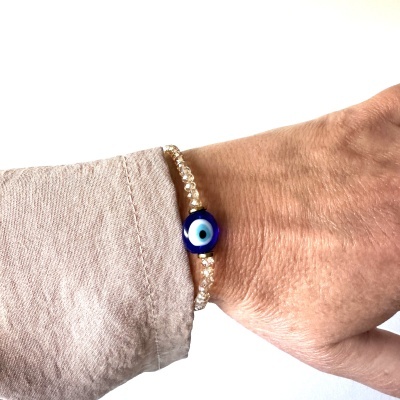 Pulseira com conta azul de olho turco e contas douradas num pulso com camisa castanho claro